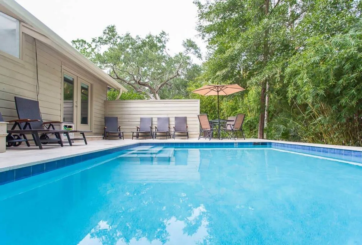 A sparkling swimming pool surrounded by comfortable lounge chairs and umbrellas, set amidst lush greenery. The tranquil poolside scene is ready for swimming, sunbathing, or outdoor dining, with hints of sunrise or sunset lighting that evoke a relaxed, resort-like vibe.