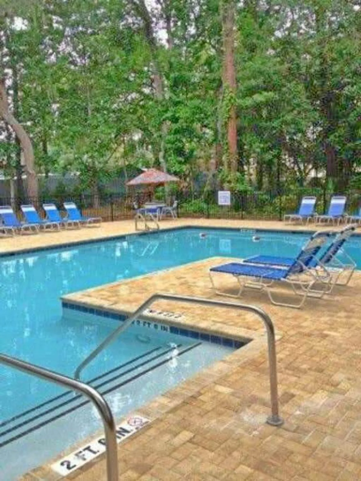 A stylish outdoor pool area with comfortable lounge chairs and a large umbrella offering shade. The scene exudes a social, resort-like atmosphere, inviting guests to swim, sunbathe, and gather for conversation and fun.