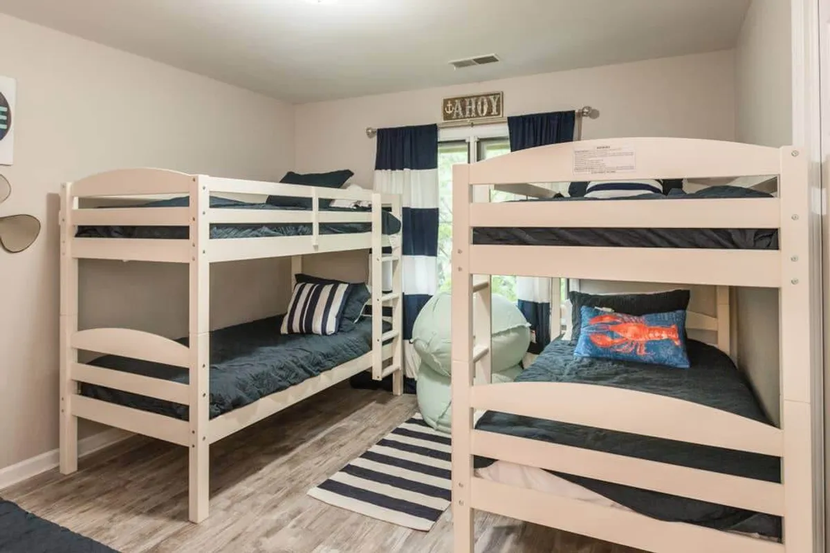 A family-friendly bedroom with bunk beds, a striped rug, a lobster pillow, and a window with curtains. The space is playful and inviting, ideal for children or groups seeking flexible sleeping arrangements.
