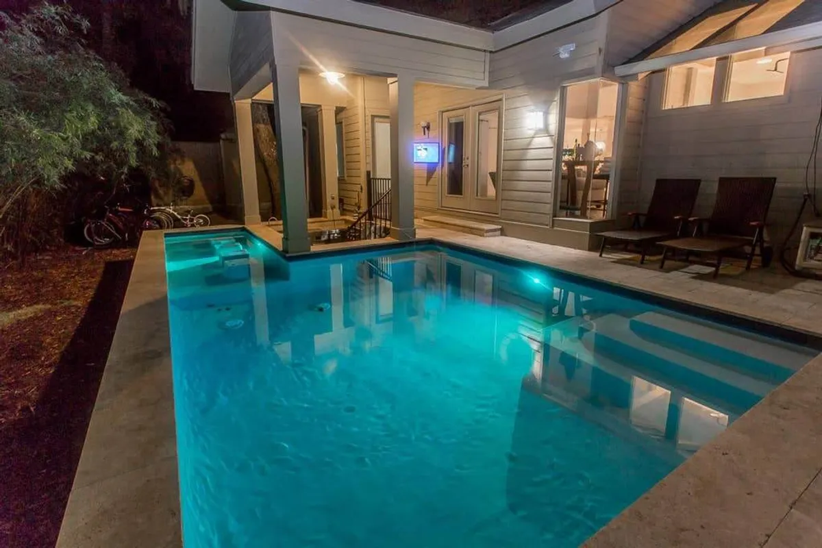 An exterior view of the pool and outdoor seating area at dusk, with the house warmly lit from within. The scene suggests evening gatherings, celebrations, or intimate family time by the water, under the stars.