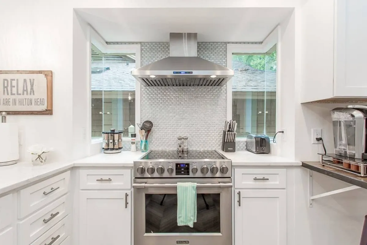 This image showcases a luxury-updated kitchen with a stainless steel range, white cabinetry, a mosaic backsplash, and kitchen utensils arrayed for use. The space is clearly designed for both functionality and aesthetics, inviting guests to cook, gather, and entertain.