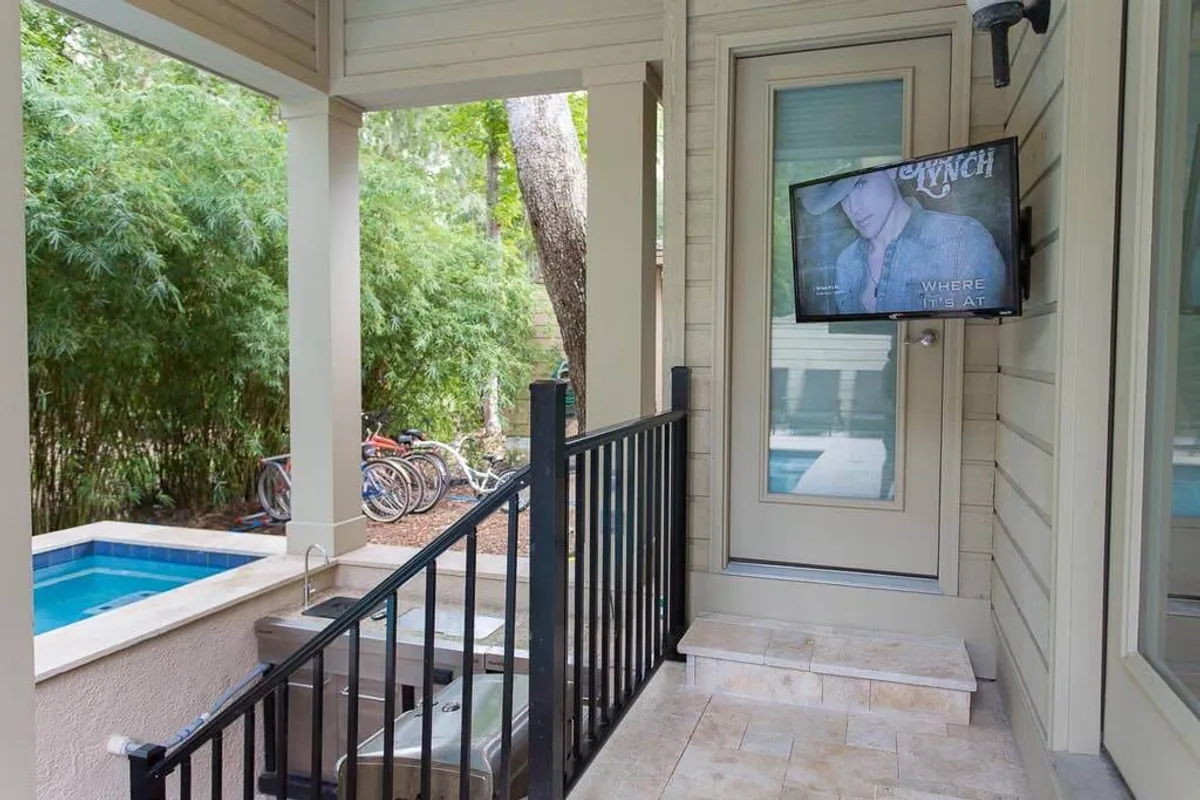 A stylish backyard scene with a swimming pool, outdoor television, lush bamboo greenery, and a modern staircase. The area is set up for both leisure and entertainment, encouraging relaxation by the water or watching movies outdoors with friends.