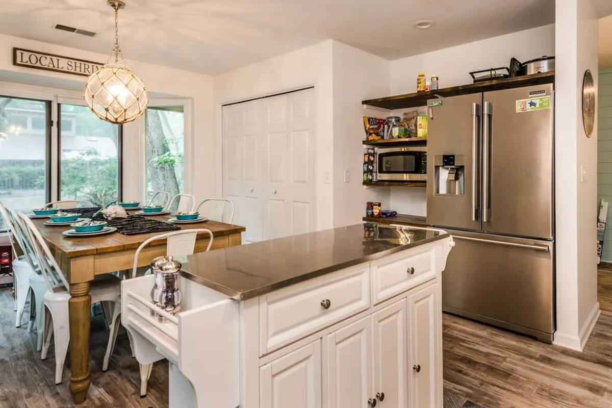 An open-concept layout featuring a dining table, kitchen island, and refrigerator. The space is designed for family meals, casual entertaining, and fluid interaction between the kitchen and dining zones. The mood is communal and inviting, with an emphasis on togetherness.