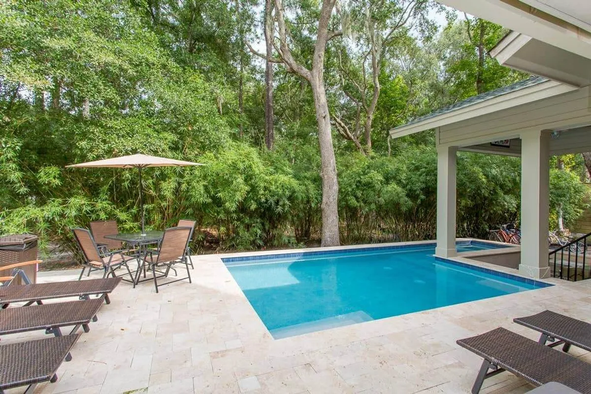 An inviting outdoor space featuring a sparkling swimming pool, a dining set for al fresco meals, lounge chairs for sunbathing, and lush greenery providing a sense of privacy and relaxation. The scene is bright and lively, ideal for both daytime enjoyment and evening gatherings.