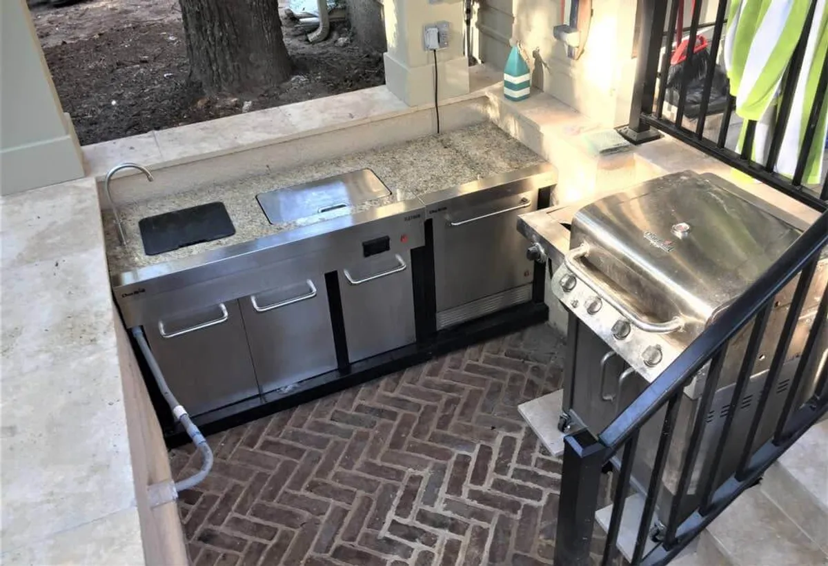 An outdoor kitchen area featuring a stainless steel grill, granite countertops, and brick flooring. The well-equipped space is designed for outdoor cooking, entertaining, and enjoying meals al fresco, embodying the social and celebratory spirit of resort communities.
