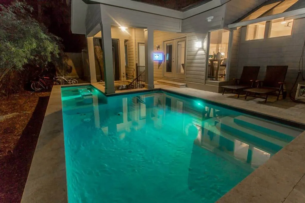 A tranquil exterior setting featuring a sparkling swimming pool surrounded by an inviting outdoor seating area. Soft lighting from the home’s illuminated windows creates a resort-like ambiance, blending relaxation with the appeal of evening social activities.